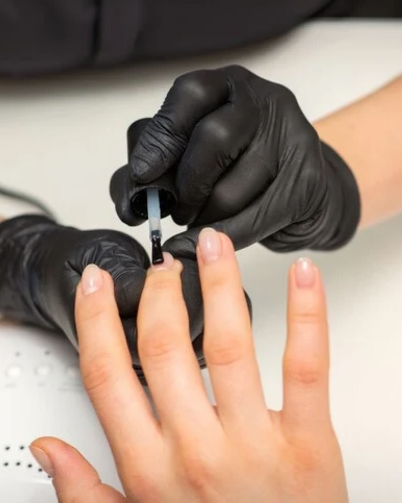Hands in black gloves applying clear nail polish to another person's nails
